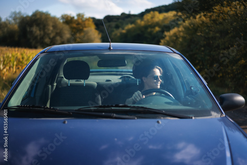 Happy young pretty woman driving a car in country side and smiling. Travel and adventure concept