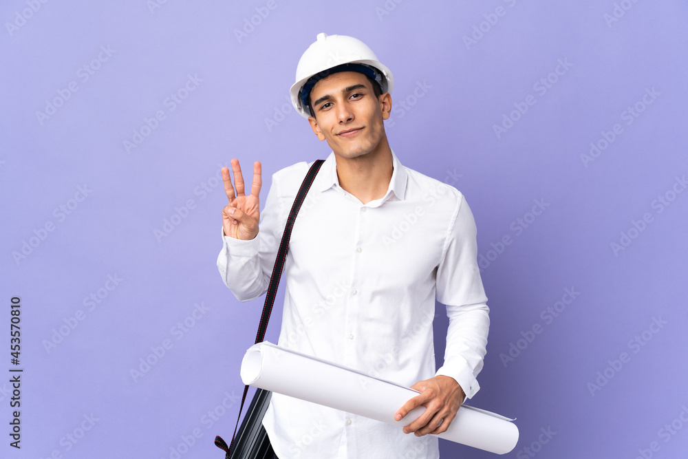 Young architect man isolated on background happy and counting three with fingers Young architect man isolated on background happy and counting three with fingers