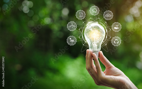 Hand holding light bulb with environment Icons over the Network connection on a green background to Technology and environmental protection, renewable, sustainable energy sources.