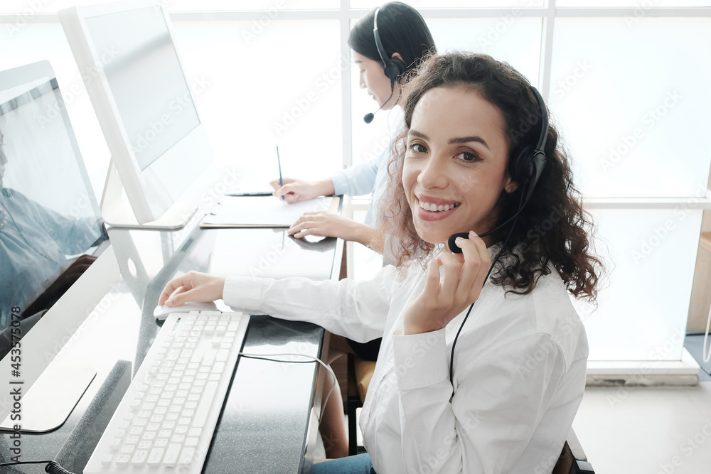Smiling caucasian and asian women are call center or secretary operator is wearing a headset and a microphone for consultant to customers. Technician Support staff for help resolve technical issues. Smiling caucasian and asian women are call center or secretary operator is wearing a headset and a microphone for consultant to customers. Technician Support staff for help resolve technical issues.