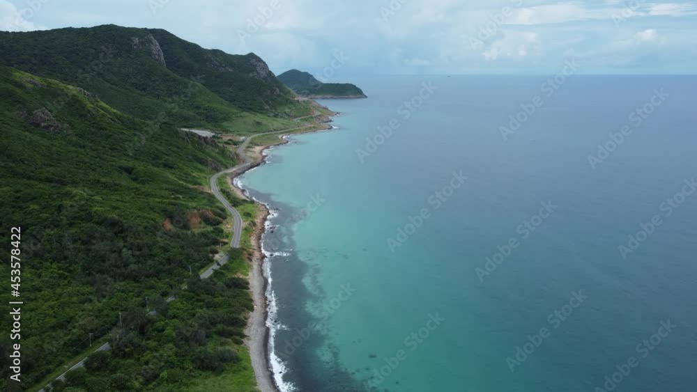 Stunning aerial view of a coastal road on the tropical island. High mountains are covered by trees. Tranquil water of the sea with fluffy clouds on the horizon. Drone footage. Vietnam, Con Dao island. Stunning aerial view of a coastal road on the tropical island. High mountains are covered by trees. Tranquil water of the sea with fluffy clouds on the horizon. Drone footage. Vietnam, Con Dao island.