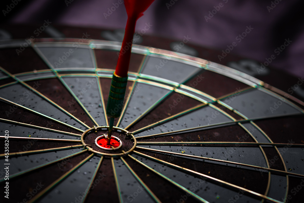 Obraz premium Close up shot of the dart arrow hit on bulleyes of dartboard to represent that the business reached the target of company with dark tone picture style. Target and goal as concept. 