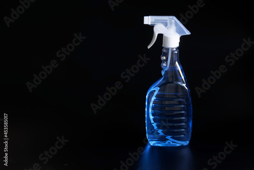 Transparent container with a spray bottle and light blue disinfectant liquid stands against a black background. The concept of cleaning from germs and viruses and disinfection