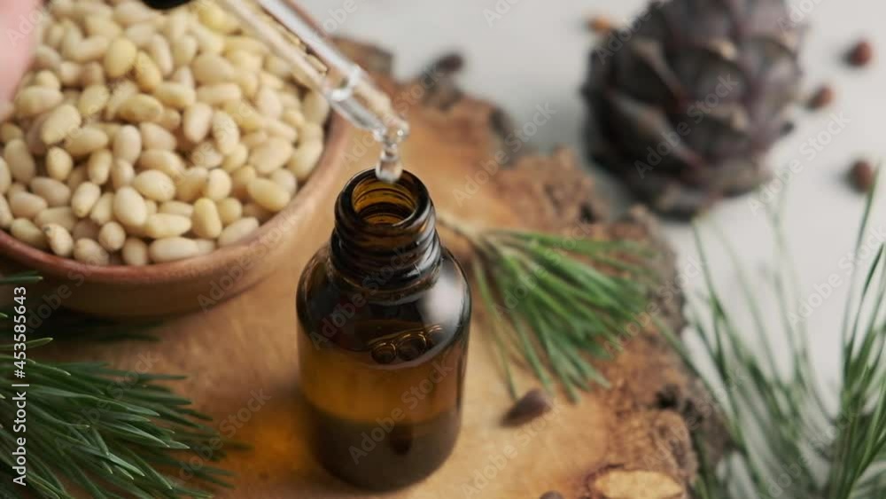 Pine essential oil with pine cones and nuts dripping from pipette to the bottle. Slow motion. Pine essential oil with pine cones and nuts dripping from pipette to the bottle. Slow motion.