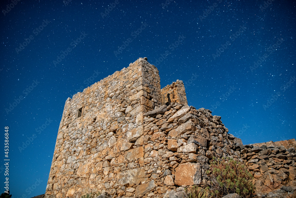 ancient stone mills and their ruins on the slopes of the mountains on the island of Crete against the background of the starry sky 