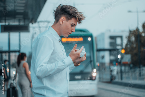 Hombre joven ejecutivo esperando al tranvía en la estación poniendose la mascarilla quirurjica photo