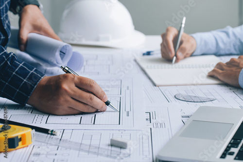 Two Architect discussing a project and working on blueprint at the construction site at desk in the office, Architectural and engineering concept.