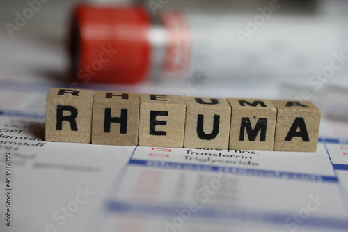 Viersen, Germany - June 1. 2021: Closeup of word rheuma on laboratory requisition slip with syringe and vial (selective focus on text blocks in center) photo