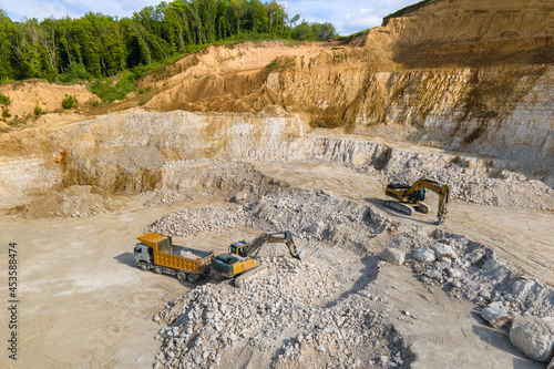Open pit mining of construction sand stone materials with excavators and dump trucks.