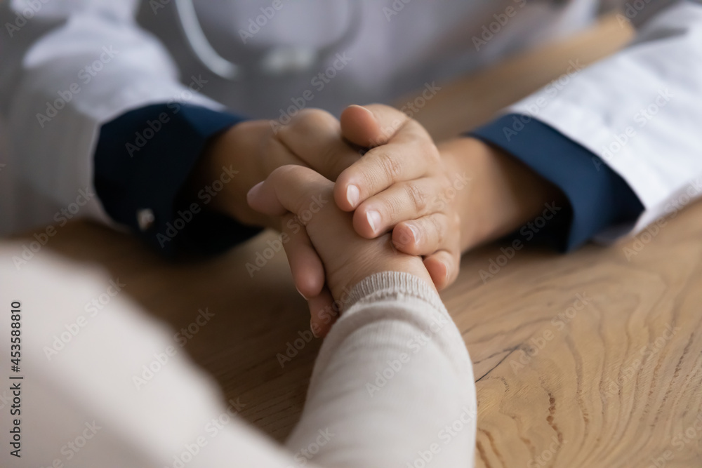 Fototapeta premium Close up kind young female psychologist general practitioner doctor holding hand of mature old woman, giving support or showing empathy during checkup meeting in hospital, mental health concept.
