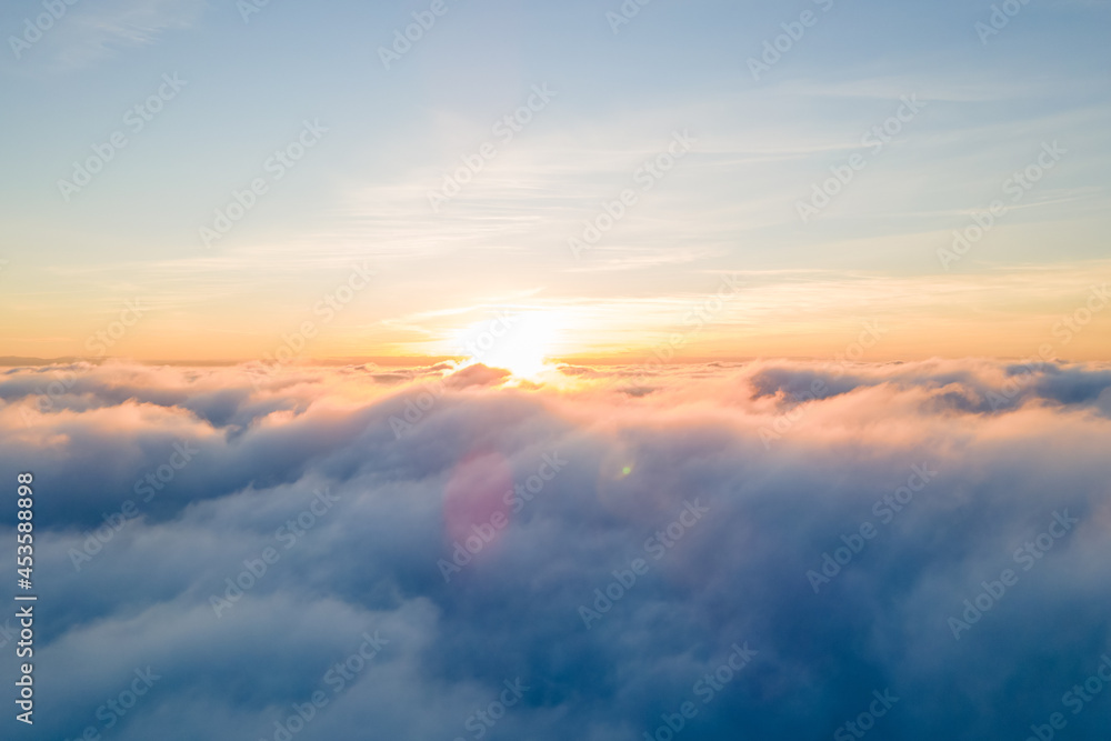 Aerial view of bright yellow sunset over white dense clouds with blue sky overhead.