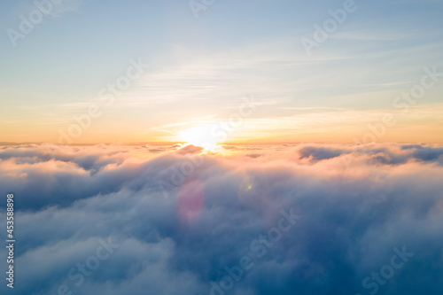 Aerial view of bright yellow sunset over white dense clouds with blue sky overhead. © bilanol