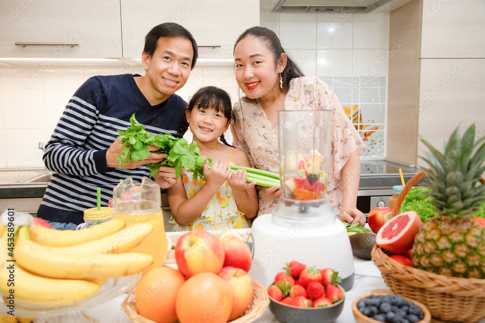 Happy asian family mother and her daughter enjoy prepare freshly squeezed fruits with vegetables for making smoothies for breakfast together in the kitchen. diet and Health food concept.