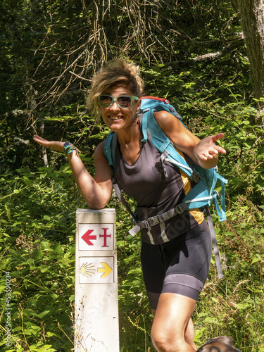 Vertical shot of a young confused hiker woman standing near a direction sign photo