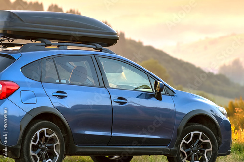 SUV car with roof rack luggage container for off road travelling parked at roadside at sunset. Road trip and getaway concept. © bilanol