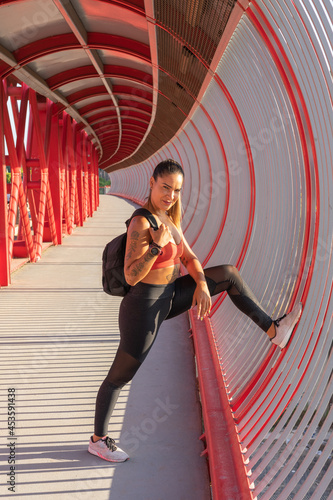 Chica deportista con la mochila de deporte, con pie apoyado en el puente, con expresión desafiante.