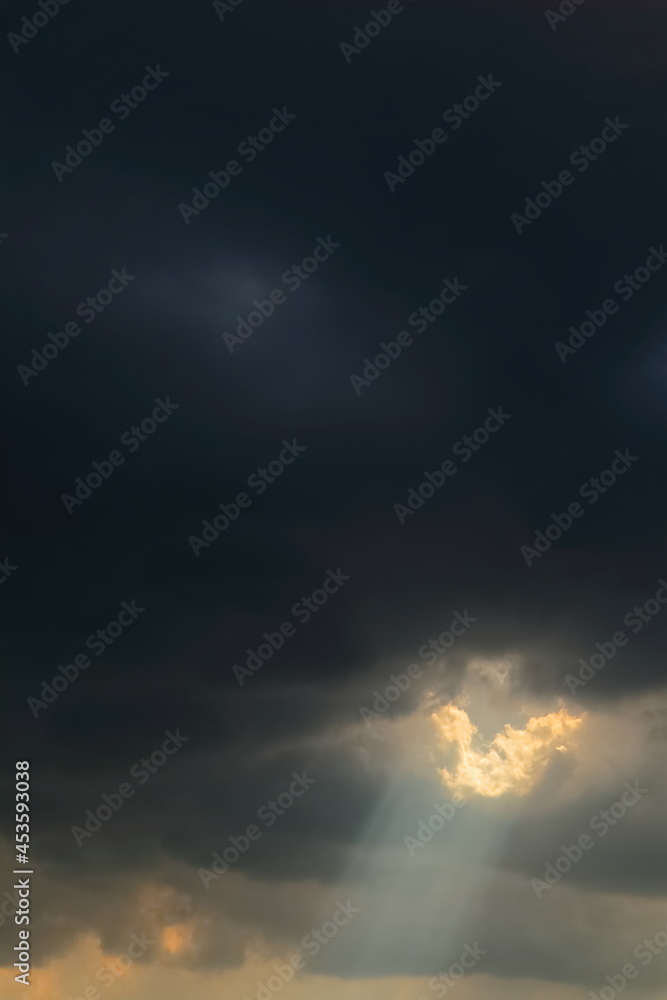 Obraz premium Sunlight breaking through storm clouds in dramatic sky. Atmospheric scene with dark tones and radiant beams of light