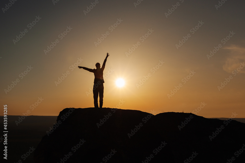 Silhouette of a man in the mountains against the background of the rising sun. The concept of freedom