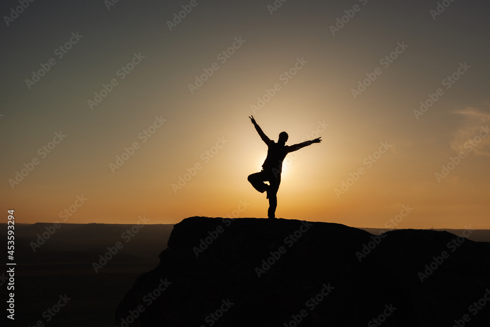 Silhouette of a man in the mountains against the background of the rising sun. The concept of freedom