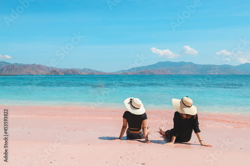 Two woman tourists in summer hat sitting and relaxing in pink sandy beach at Labuan Bajo
