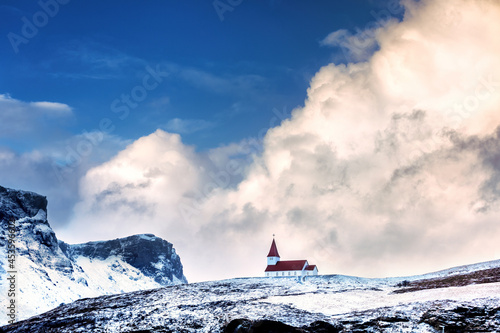 Canvas Vik i Myrdal church, in Vik, Iceland, against snowy mountains and blue sky with rolling clouds
