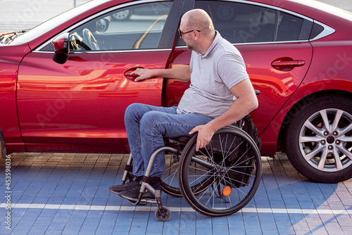 Young handicapped driver getting in red car fom wheelchair