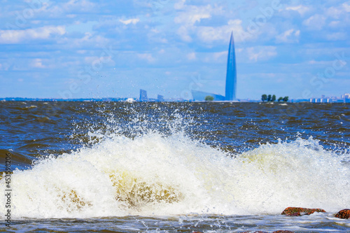 Gulf of Finland Baltic Sea in sunny summer day, waves break on the coastal stones. Lakhta center on background, Saint Petersburg, Russia photo