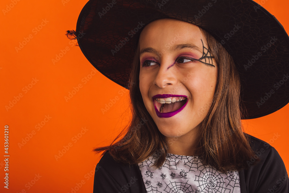 Portrait of a very smiling little witch against an orange background on Halloween Portrait of a very smiling little witch against an orange background on Halloween