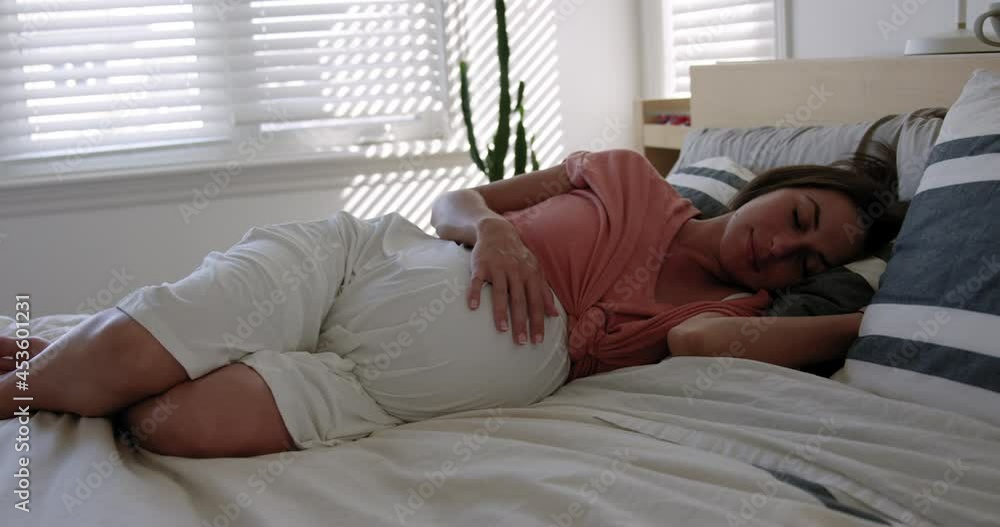 Third trimester Pregnant woman rubs belly as she takes day nap - wide shot Third trimester Pregnant woman rubs belly as she takes day nap - wide shot
