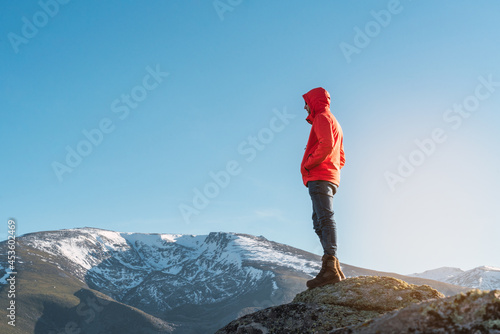Unrecognizable hiker dressed in a red coat standing on top of a snowy mountain looking at the view