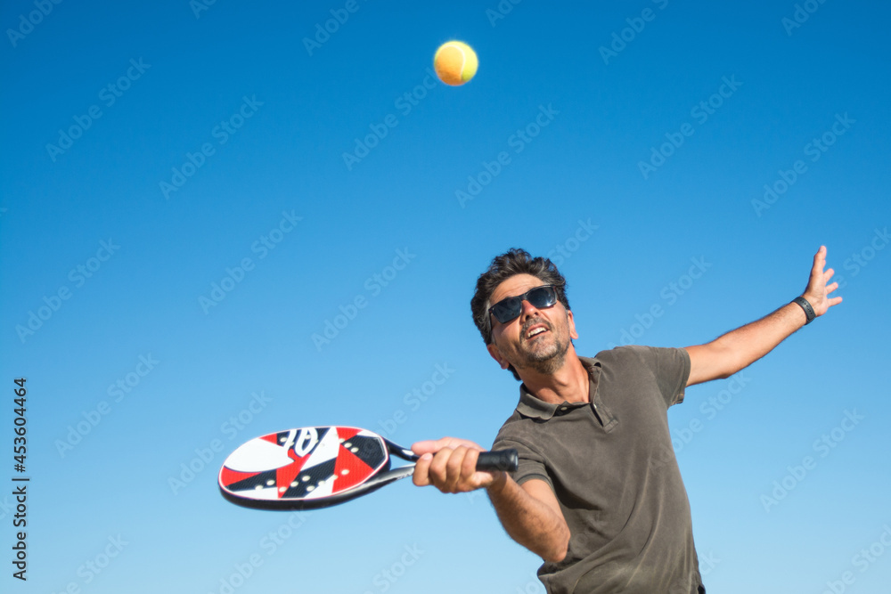 Foto de Man Holding A Paddle Tennis Racket Hitting The Ball On A Blue