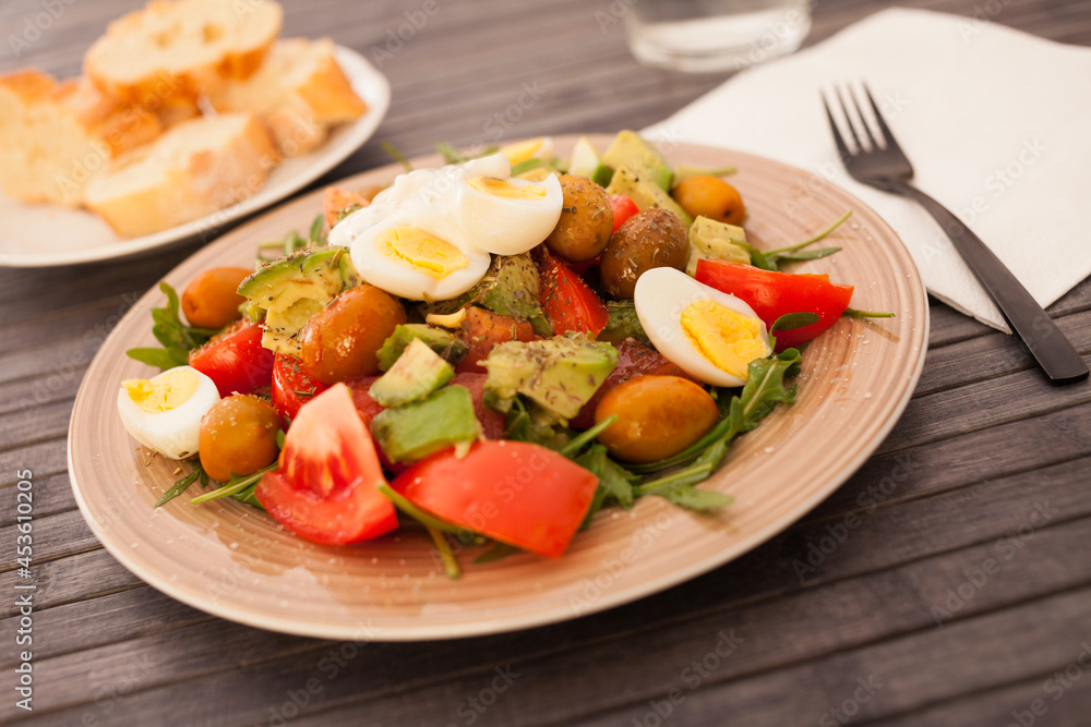 fresh salad of arugula, avocado, cherry tomatoes with olives and quail eggs on brown plate fresh salad of arugula, avocado, cherry tomatoes with olives and quail eggs on brown plate