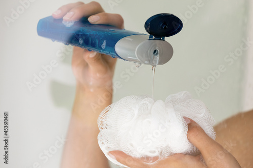 Фотография Close up young woman pouring liquid moisturizing soap shower gel from cosmetic bottle on loofah puff, enjoying morning evening body cleansing routine, removing dead cells exfoliating in bathroom