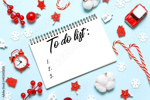 To do list in notepad with christmas decorations on blue background. Flat lay, top view, copy space. New year winter holiday xmas concept