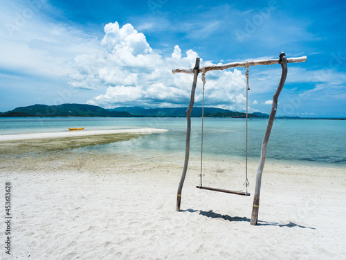 Wooden swing and yellow kayak on white sand beach tropical island against mountain and fluffy cloud blue sky background. Koh Mat Sum Island, Near Koh Samui, Thailand.
