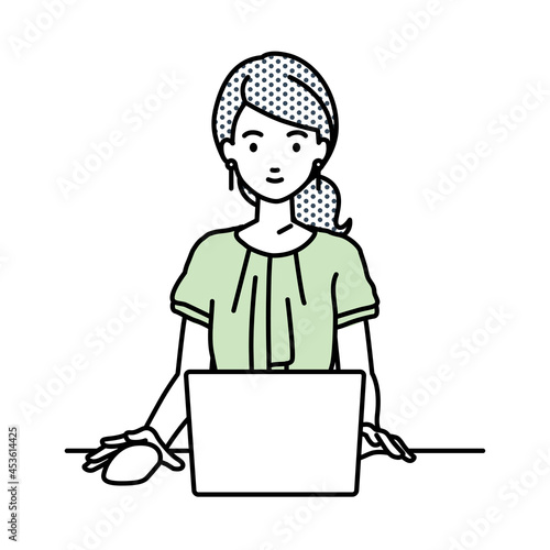デスクで座ってPCを使っているオフィスカジュアルの女性