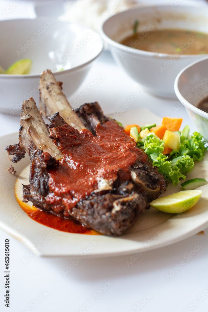 top view of grilled beef ribs with vegetables pickles and brown soup in plate