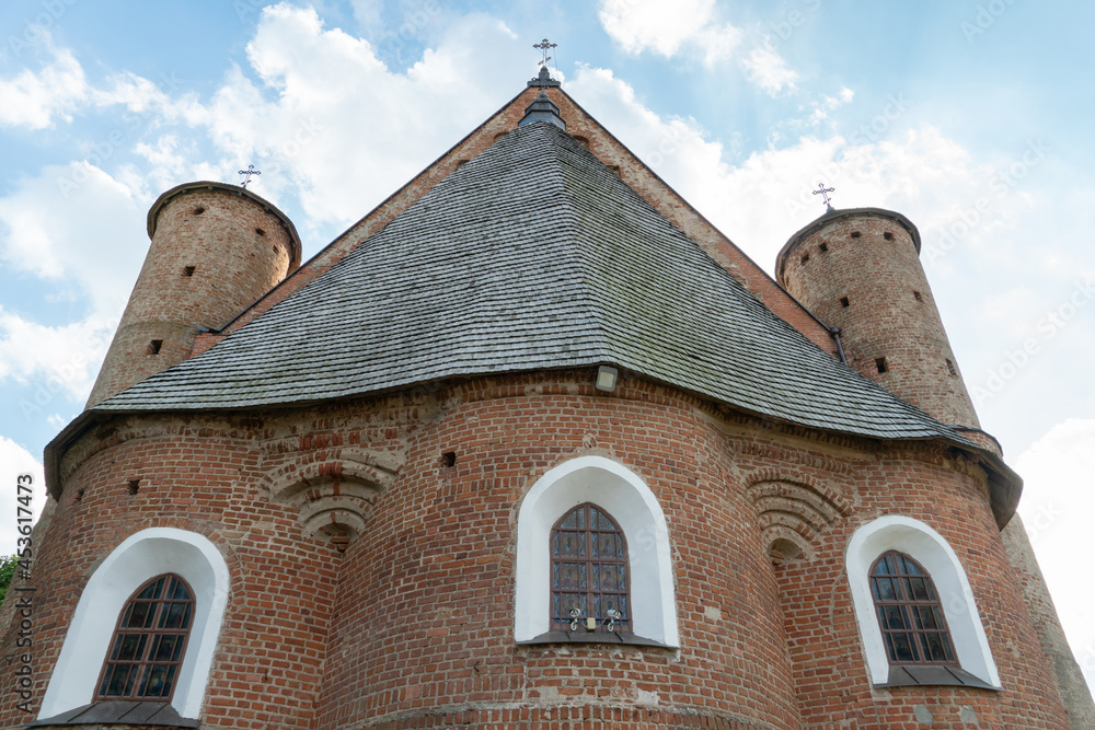 Fototapeta premium A beautiful old fortress church made of red brick against a blue sky background. Beautiful tiled roof of a medieval castle and white arched windows.