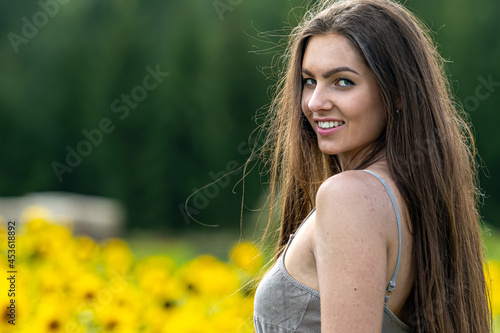 young woman with long hair in linean country style dress walks through a field of sunflowers photo