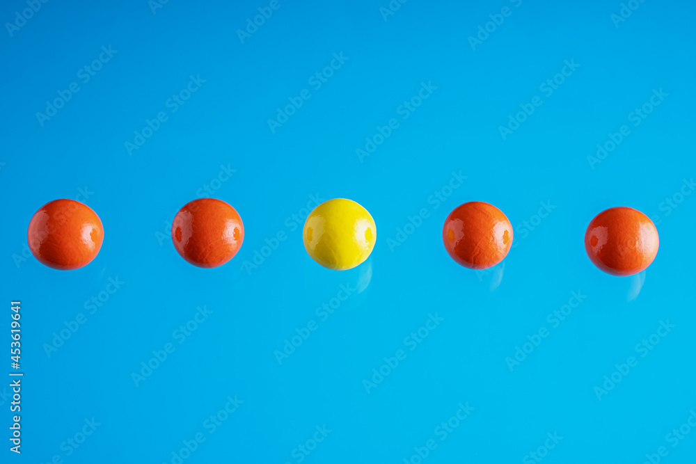 Conceptual row of red balls with a one yellow ball standing on blue background. The concept of unique and different Conceptual row of red balls with a one yellow ball standing on blue background. The concept of unique and different