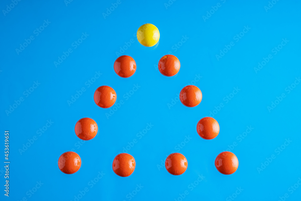 Naklejka Pyramid of red spheres and a yellow one on top of it on blue background.