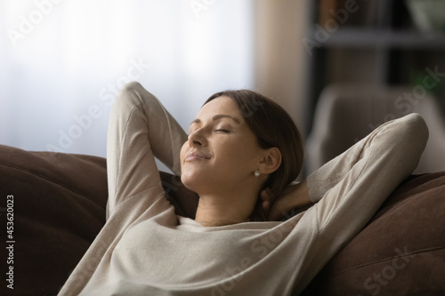 Close up peaceful woman with closed eyes relaxing on cozy couch at home, calm mindful sleepy young female leaning back, visualizing good future, taking nap or daydreaming, enjoying leisure time © fizkes