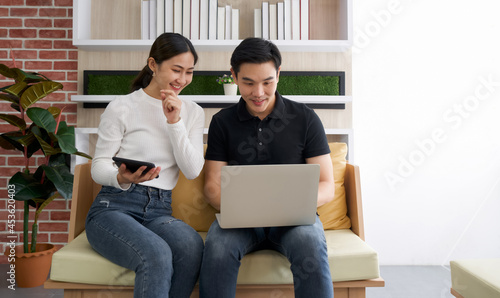 Young lovers spend time together on holidays in the living room. Both of them are interested in internet product information while the man held laptop computer.
