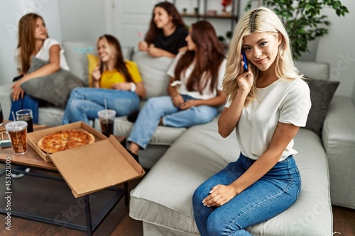 Group of young friends woman eating italian sitting on the sofa. Girl smiling and talking on the smartphone at home.