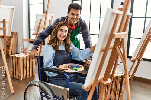 Teacher and disabled paint student sitting on wheelchair smiling happy painting at art school.
