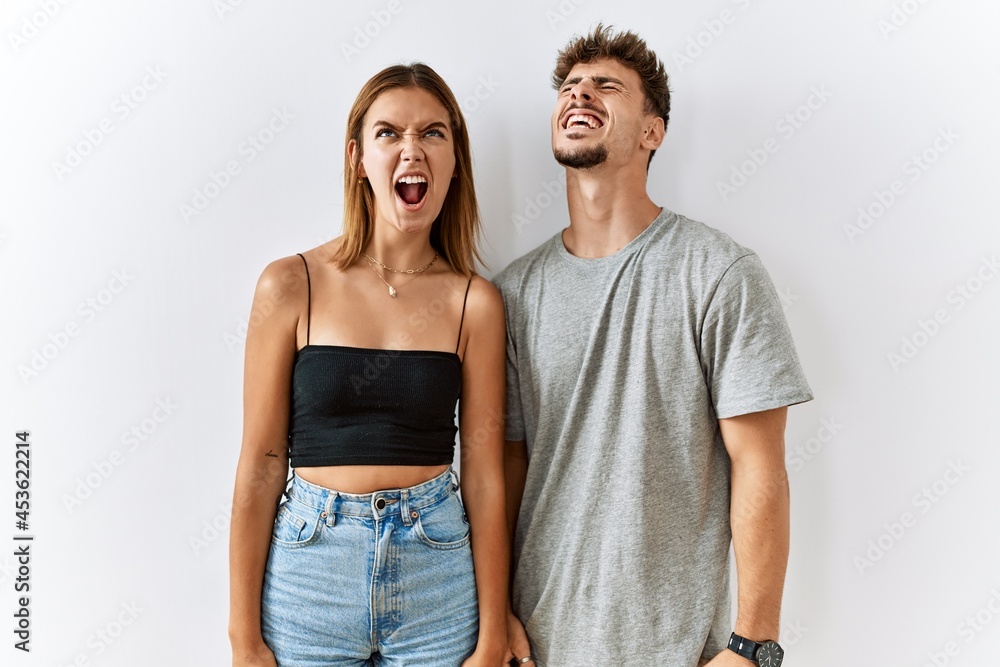 Naklejka premium Young beautiful couple standing together over isolated background angry and mad screaming frustrated and furious, shouting with anger. rage and aggressive concept.