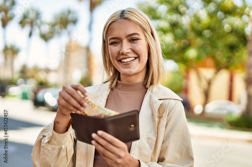 Young blonde girl smiling happy holding wallet with norway krone banknotes at the city.