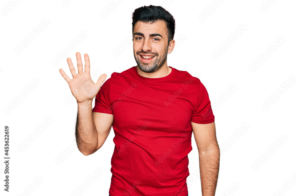 Hispanic man with beard wearing casual red t shirt showing and pointing up with fingers number five while smiling confident and happy. Hispanic man with beard wearing casual red t shirt showing and pointing up with fingers number five while smiling confident and happy.