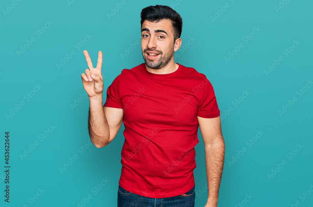 Hispanic man with beard wearing casual red t shirt showing and pointing up with fingers number two while smiling confident and happy. Hispanic man with beard wearing casual red t shirt showing and pointing up with fingers number two while smiling confident and happy.