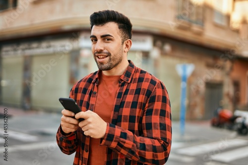 Young hispanic man smiling happy using smartphone at the city.